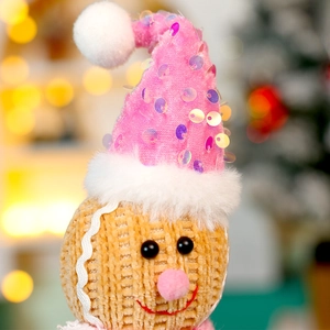 Macro shot of knitted gingerbread doll head with pink sequined hat and bokeh background