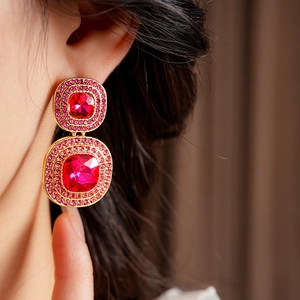 Close-up of vintage gold square earrings with red stones and pink crystals on a model