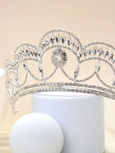 Detail view of ornate silver bridal crown with sparkling clear rhinestones on white pedestal