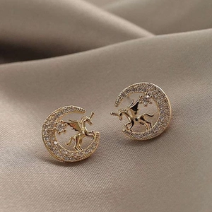 Macro detail of gold moon and winged unicorn stud earrings with sparkling white zircons