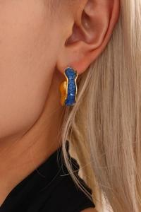 Detailed view of C-shaped gold-plated earring with blue crystal stones on model
