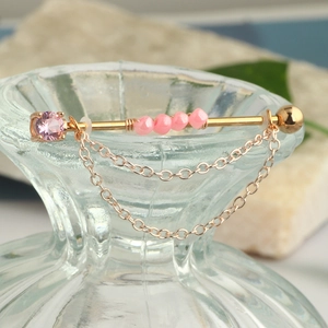 Detail view of golden industrial piercing with pink gemstones and hanging chains