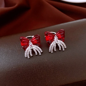 Detail of red bow earring with cubic zirconia tassel on dark brown textured surface