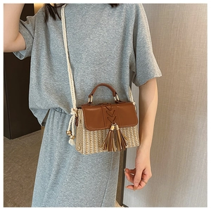 Detail of straw woven crossbody bag with brown leather flap and stylish tassel accents