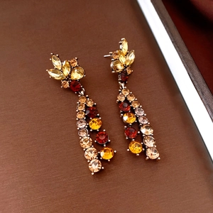 Detail of vintage flower earrings with yellow, orange, and red crystals on wood