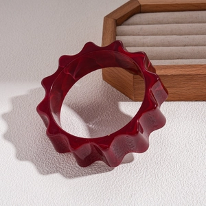 Macro detail of dark red wavy acrylic bangle with marble texture on white surface