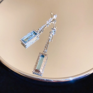 Macro shot of light blue geometric crystal earrings with silver chain on mirror base