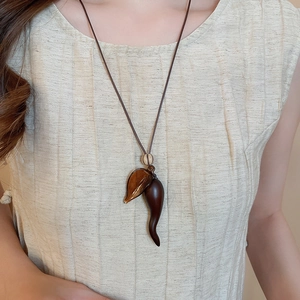 Detail of retro resin chili pendant necklace with leaf charm and woven cord on a model