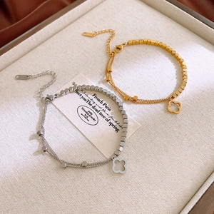 Close-up of gold and silver steel clover charm bracelets on a textured display tray