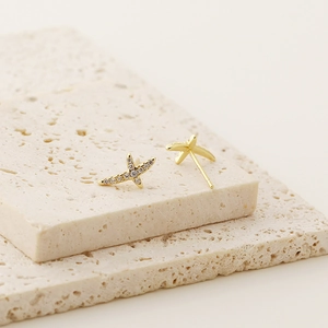 Macro detail of gold-plated cross stud earrings with sparkling cubic zirconia inlay