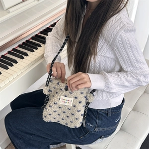 Close-up of plush cream crossbody bag with blue heart pattern and striped woven strap