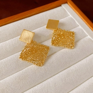 Close-up of golden square earrings featuring brushed metal and woven mesh texture