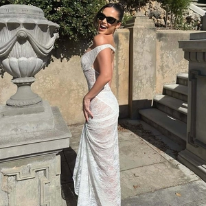 Detail of white lace sleeveless maxi dress with sexy open back standing near stone wall