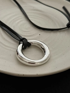 Close-up of a silver mirror ring pendant on a black leather cord over a ceramic plate