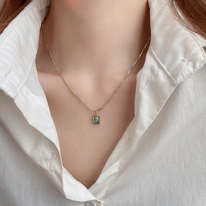 Detail of gold necklace with square turquoise pendant and small green beads on a model