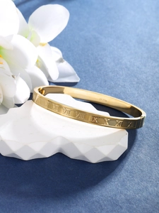 Detail of gold metal bangle featuring Roman numerals engraving on polished flat surface