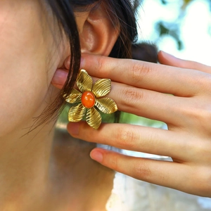 Detail of vintage gold flower earring with orange stone on female model ear