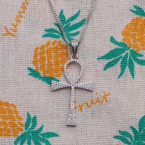 Silver Ankh cross necklace with zircon stones and metal box chain on patterned fabric