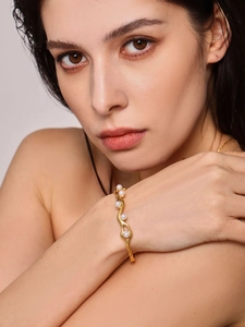 Detailed view of an 18K gold-plated wavy C-shaped bangle with white pearls on wrist