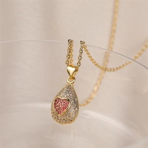 Détail du pendentif goutte dorée avec cœur rouge sur fond de tissu en soie beige
