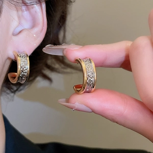 Detail of 18k gold plated C-shaped hoop earrings with silver lava textured inlay