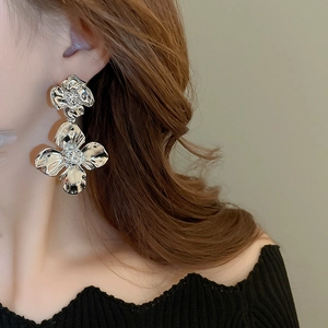 Detailed view of oversized silver floral earrings with layered metallic petals on model