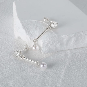 Macro detail of asymmetric silver earring with shiny zircon stud and dangling white pearl