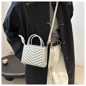 Silver quilted handbag with V-shaped stitching and top handle shown on a model