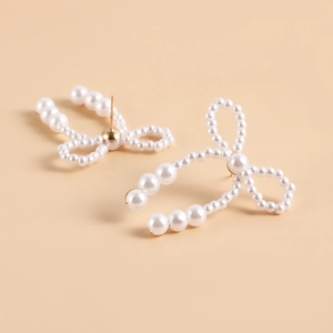 Close-up of handmade white pearl bow earrings with gold metal accents on beige background