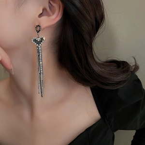 Detail view of heart-shaped emerald diamond earrings with long tassels on a model