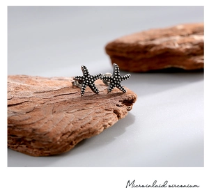 Macro shot of silver starfish stud earring with micro inlaid zirconium on rustic bark