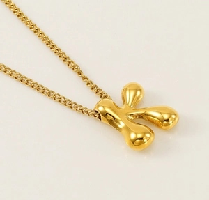 Macro view of a 3D bubble letter K pendant in polished gold finish with a delicate chain