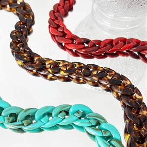 Macro detail of chunky acrylic chain necklaces in red, amber, and turquoise textures