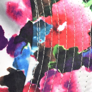 Close-up of vibrant floral tie-dye fabric featuring precise white stitching detail