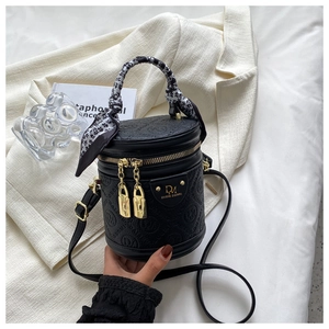 Close-up of black cylindrical handbag with floral scarf handle and gold hardware