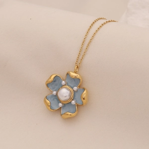 Gold chain necklace with blue flower pendant featuring pearls on a soft fabric background