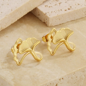 Detailed view of golden ginkgo leaf stud earrings resting on a textured beige stone surface