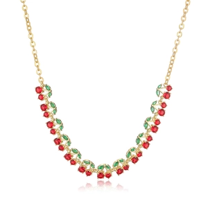 Elegant gold cherry necklace with red and green crystals on a white reflective surface