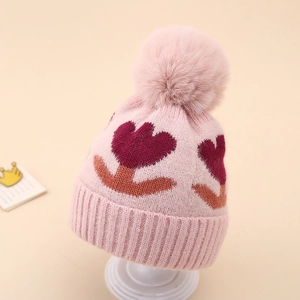 Detail of pink knitted baby beanie with fluffy pompom and tulip flower pattern design