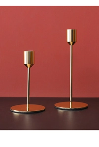 Detail von zwei modernen goldenen Kerzenhaltern auf dunklem Holztisch vor rotem Hintergrund