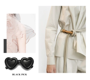 Detail shot of black heart-shaped polarized sunglasses with a beige braided belt accessory