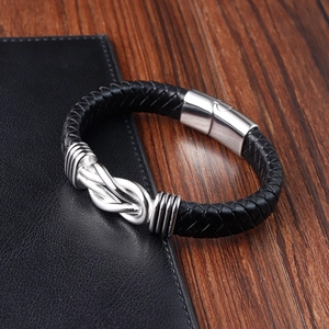 Macro shot of black braided leather bracelet with silver infinity knot on leather notebook