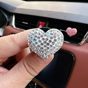 Close-up of sparkling heart-shaped rhinestone car air vent clip being held by a hand