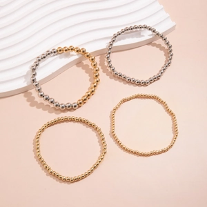 Detail of four metallic beaded bracelets in gold and silver finish on a beige background