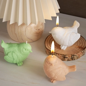Three bird shaped candles with detailed feathers on a rustic wooden base in a warm room