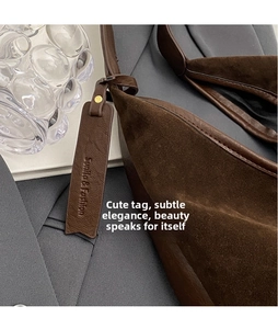Detailed close-up of dark brown suede tote bag with decorative leather tag and smooth trim
