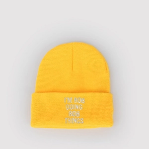 Detail of bright yellow knit beanie featuring I'M BOB DOING BOB THINGS white embroidery