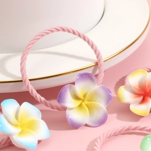 Elastic kids hair ties with colorful frangipani flower ornaments on pink surface