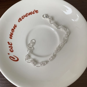 Minimalist S925 sterling silver woven link chain bracelet on a decorative ceramic tray
