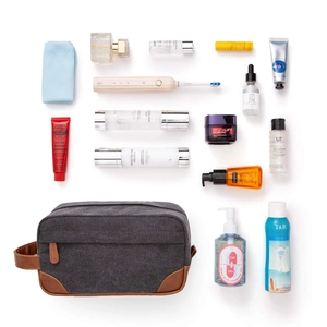 Grey canvas toiletry bag with brown leather trim and grooming accessories on white